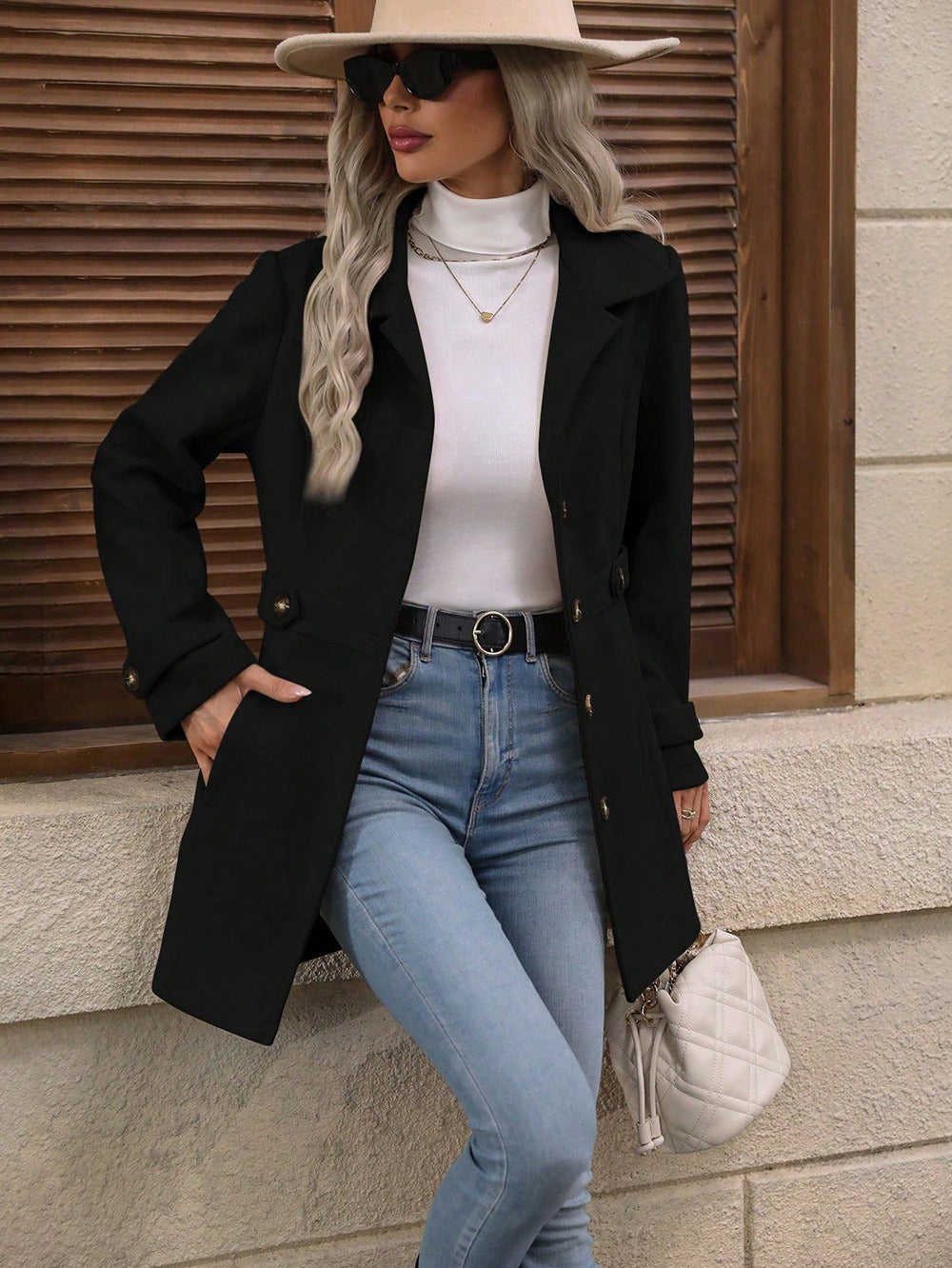 Woman in black coat, white turtleneck, light blue jeans, beige hat, black sunglasses, and white quilted handbag