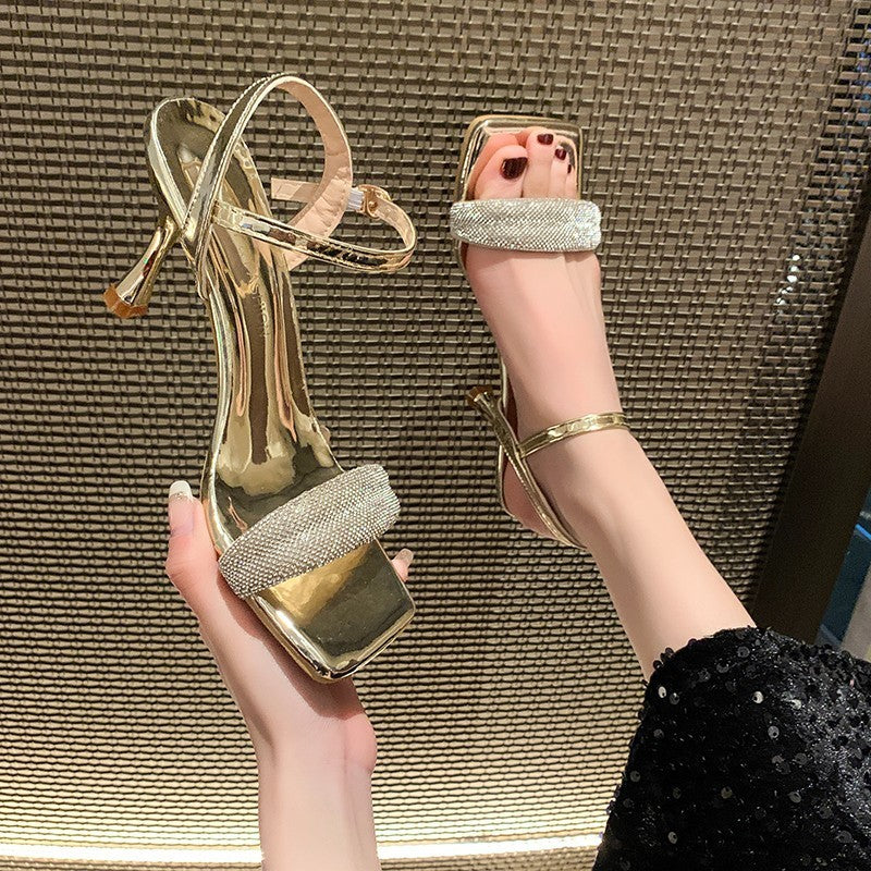 gold high heel sandals with rhinestone straps on foot and held in hand over woven background