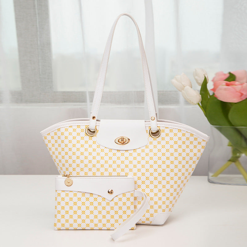 White and gold patterned handbag and matching wristlet on white table with flowers in background