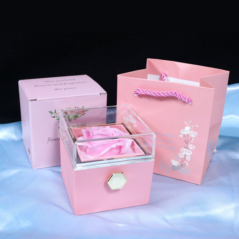 Pink gift box with clear lid showcasing a pink artificial rose, accompanied by matching floral gift bag and packaging