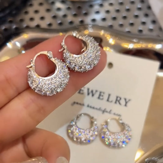 Hand holding pair of silver hoop earrings encrusted with sparkling crystals on jewelry card