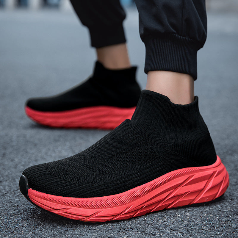 Black sock-style sneakers with textured red thick soles worn on asphalt