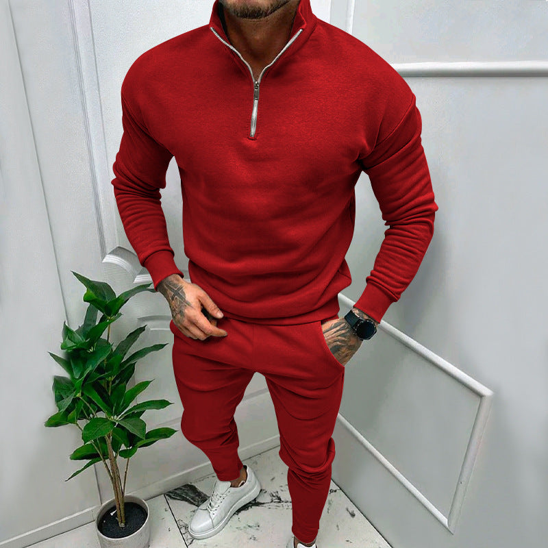 Man wearing a red zip-up sweatshirt and matching joggers with white sneakers in minimalist room