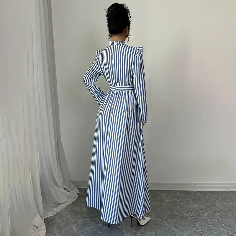 Back view of woman in blue and white vertical striped long sleeve maxi dress with ruffled shoulders and white heels