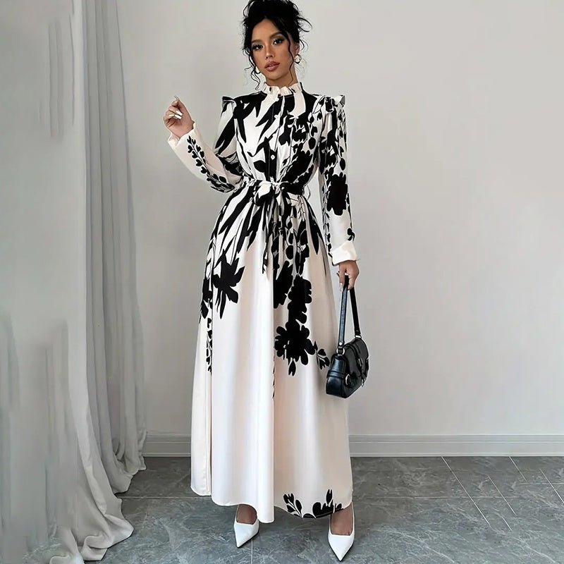 Woman wearing black and white floral print long sleeve maxi dress with stand collar and waist tie, holding black handbag
