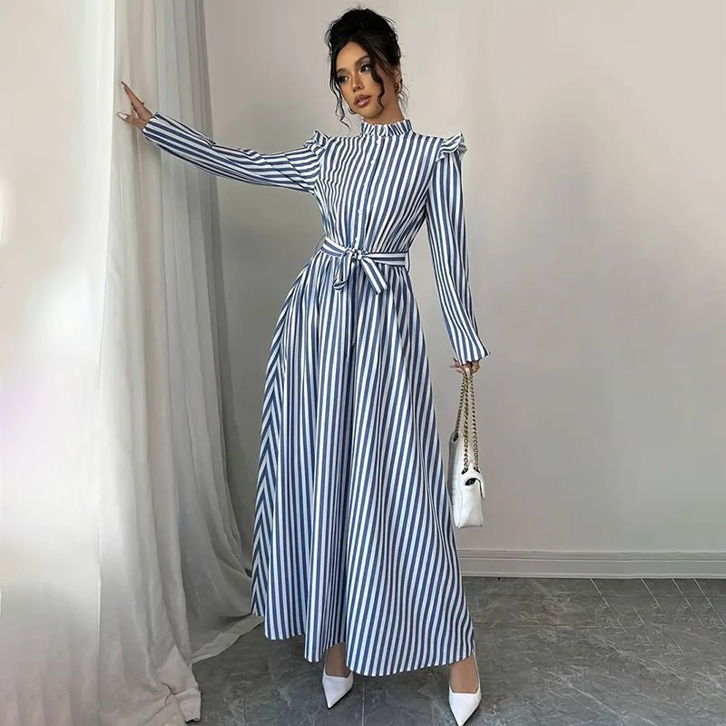Woman wearing blue and white vertical striped long sleeve maxi dress with waist tie, standing indoors