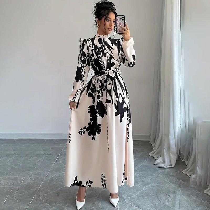 Woman wearing black and white floral print long sleeve maxi dress with stand collar and waist tie posing indoors