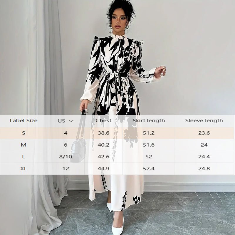 woman wearing black and white floral long sleeve maxi dress with stand collar and waist tie in a minimalist room