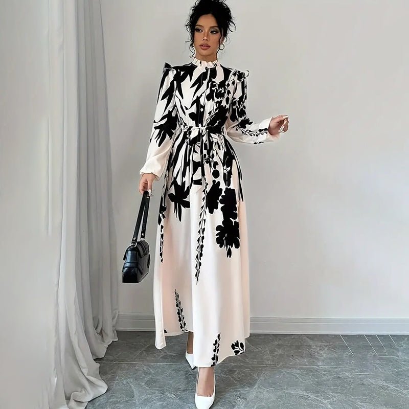 Woman wearing black and white floral print long sleeve maxi dress with stand collar and waist tie, holding black handbag