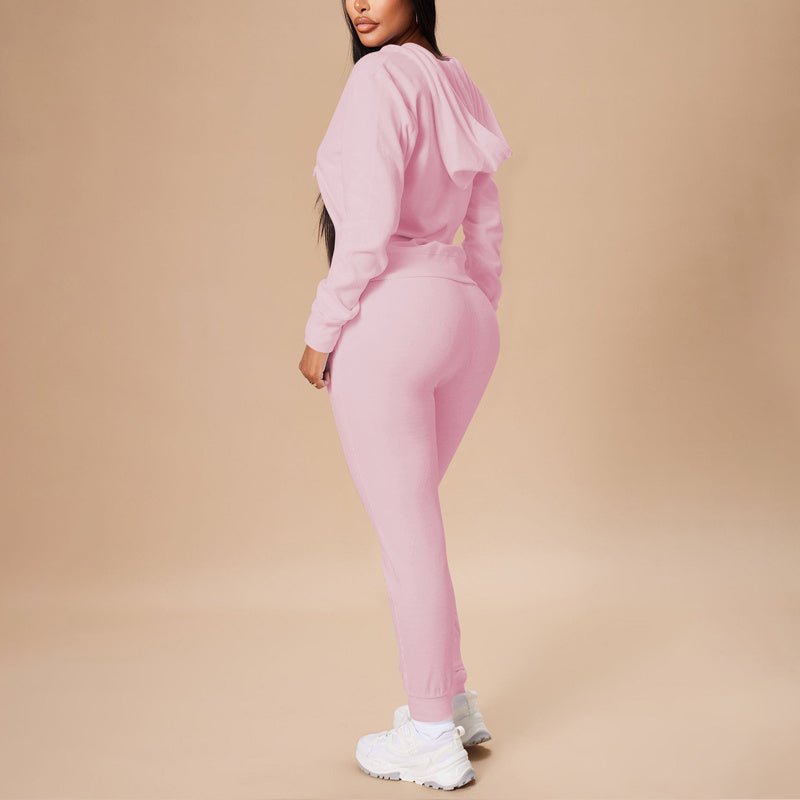 Woman wearing a pink ribbed two-piece casual set with hooded crop top and slim-fit pants, white sneakers