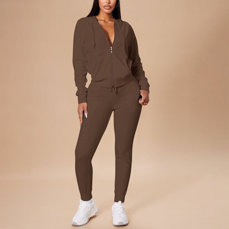 woman wearing brown hooded zip-up crop top and slim fit pants set with white sneakers on beige background