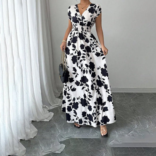 Woman wearing white wrap V-neck maxi dress with black floral print and elastic waist, holding black handbag