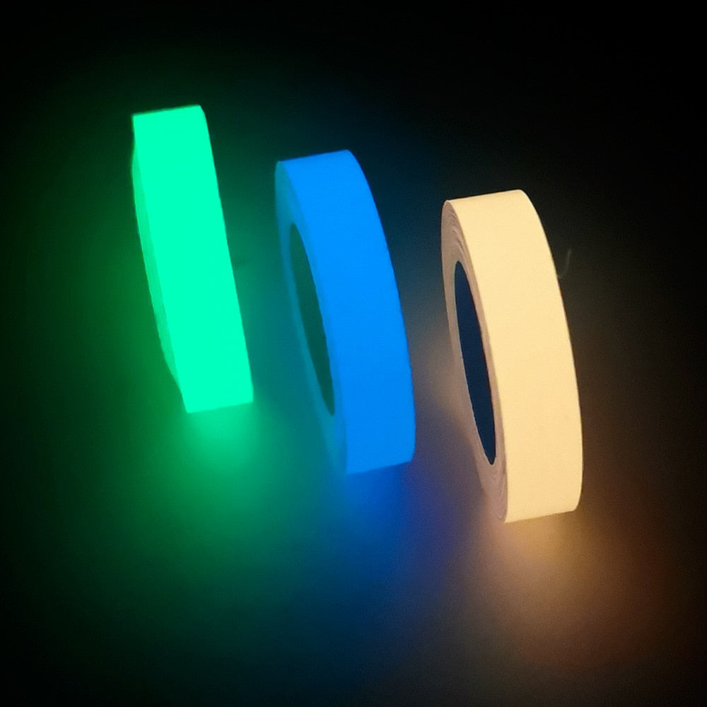 Three rolls of glowing adhesive tape in green, blue, and yellow on a dark surface