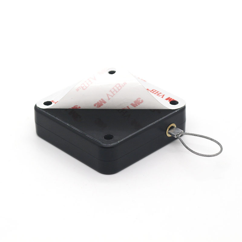 Black square security tag with adhesive backing partially peeled and attached metal wire loop